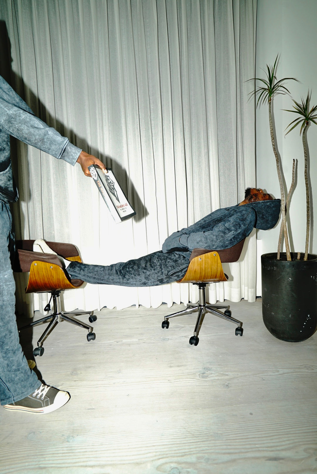 LX3 campaign photograph of a model reclining across chairs in a washed denim set